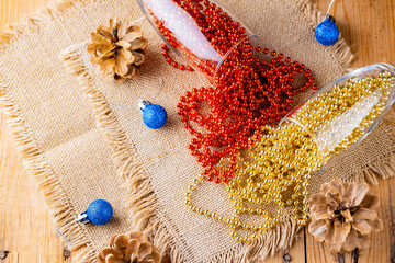 Two champagne glasses with Christmas beads. Christmas balls and decorations on sackcloth. Pine cones and multicolored beads on wooden background. Top view