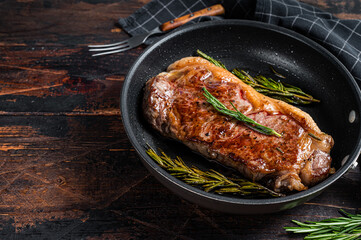 Grilled new york strip beef meat steak in a pan with herbs. Dark wooden background. Top view. Copy...