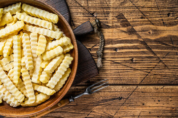 Cold Frozen Crinkle oven French fries potatoes sticks in a wooden plate. Wooden background. Top view. Copy space