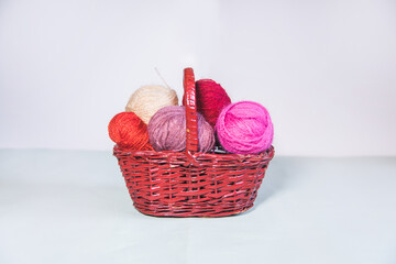 Conjunto de ovillos de lana rosa en una cesta de mimbre sobre fondo blanco. Agujas de tejer. Crochet, ganchillo. Bolas de hilo. Madejas - obrazy, fototapety, plakaty