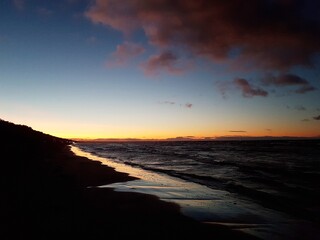 Fototapeta premium Small wave on the surface of the sea and a dark sandy beach against the blue sky after sunset