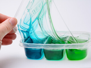 A transparent plastic container with multicolored slides opens with a hand, close-up on a gray background