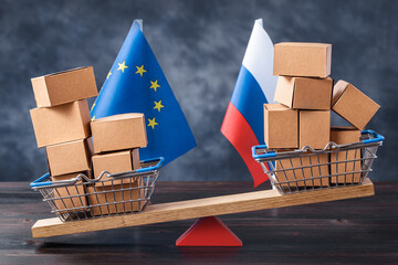 Filled shopping basket and cart with Russia and EU flags on seesaw. Trade balance concept