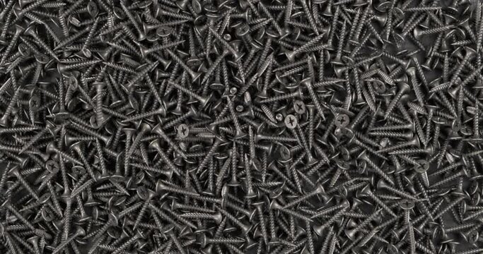 Rotation. Falling screws onto a pile of black screws. Industrial background.