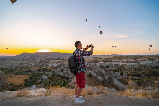 Man takes a picture, photo on smartphone. Tourist attraction balloon flight on background. Entertainment, tourism an vacation. Travel tour. Goreme, Cappadocia, Turkey.