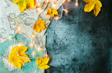 Yellow leaves, geographic map and glowing garland on a concrete background