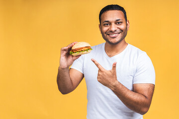 Young african american indian black man eating hamburger isolated over yellow background. Cook preparing burger.