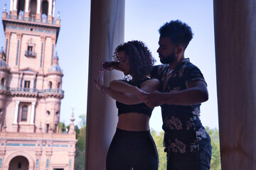 Multi-ethnic young couple doing figures while dancing bachata sensually outdoors.