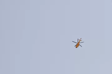 Fotobehang High view of a yellow helicopter flying with clear blue sky © Diana Samson/Wirestock