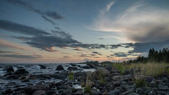 4K time lapse of Magnificent Soft and colorful sunset by the seaside stone. Beautiful cloud movement with seashore stones. Gradual light reduction.