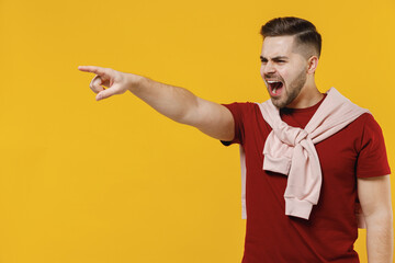 Young stressed strict angry man 20s in red t-shirt casual clothes point index finger aside scream shout do it isolated on plain yellow color wall background studio portrait. People lifestyle concept