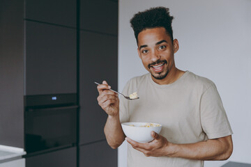 Young fun cool satisfied african american man 20s in casual clothes eat breakfast muesli cereals...