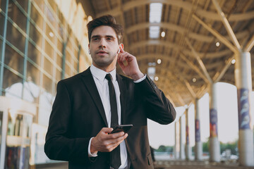 Bottom view traveler businessman man wearing black dinner suit earphones stand outside at international airport terminal speak on mobile phone book taxi order hotel Air flight business trip concept