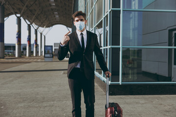 Young traveler european businessman man 20s wear black dinner suit point finger on facial mask walk...