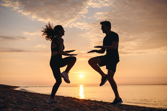 Full body side view couple young friends sporty sportsman woman man in sport clothes warm up training jumping do exercise on seaside sunrise over sea sand ocean beach outdoor in summer day morning