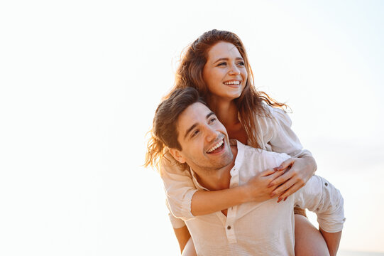 Close up young happy enamored smiling couple two friends family man woman in casual clothes boyfriend give piggyback ride to joyful, girlfriend sit on back look aside on light white sky background.