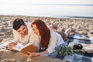 Smiling sunlit young couple two family man woman in white clothes hug lying on picnic plaid read book rest relax together at sunrise over sea beach ocean outdoor seaside in summer day sunset evening.