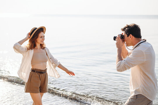 Side view happy fun young couple two family man woman in white clothes boyfriend take photo on camera of girlfriend rest date at sunrise over sea sand beach ocean outdoor seaside in summer day sunset.