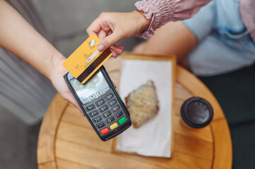 Close up young woman female hands at cafe buy breakfast food croissant and coffee beverage hold wireless modern bank payment terminal to process acquire credit card payments at store checkout indoors.