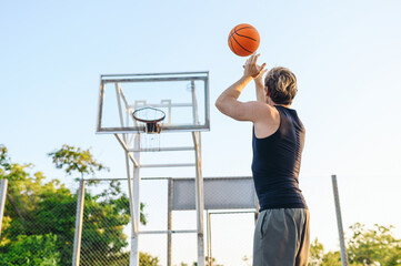 Young rear view winner sporty sportsman man in sports clothes clench fist train scoring basket shoot free throw jump play with ball at basketball game playground court Outdoor courtyard sport concept