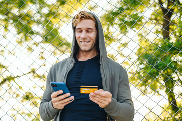 Young satisfied happy fun wistful man 20s wearing grey sportswear hood using mobile cell phone hold...