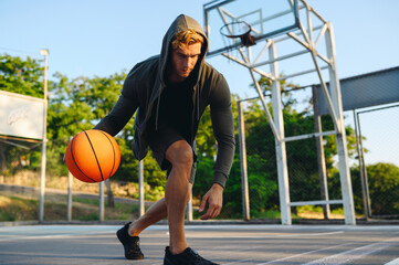 Young sporty strong confident caucasian serious sportsman man 20s wear grey dark sportswear clothes dribbling training with ball at basketball game playground court. Outdoor courtyard sports concept