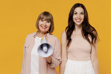 Two young satisfied smiling happy daughter mother together couple women wear casual clothes hold scream in megaphone announces discounts sale Hurry up isolated on plain yellow color background studio