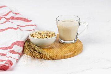 Glass of oat milk with oat flakes on white wooden background