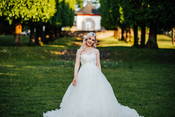 beautiful, blond bride standing and smiling in the park with a big, white dress