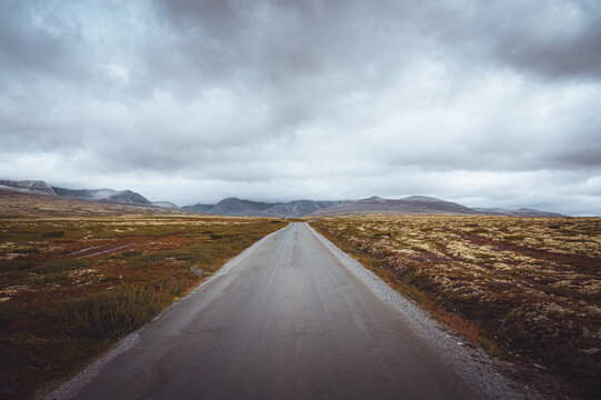 A long straight road in the Rondane National Park, Norway leading to the horizon under a cloudy sky.