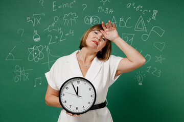 Tired teacher mature elderly lady woman 55 wear white shirt hold wall clock put hand on head has...