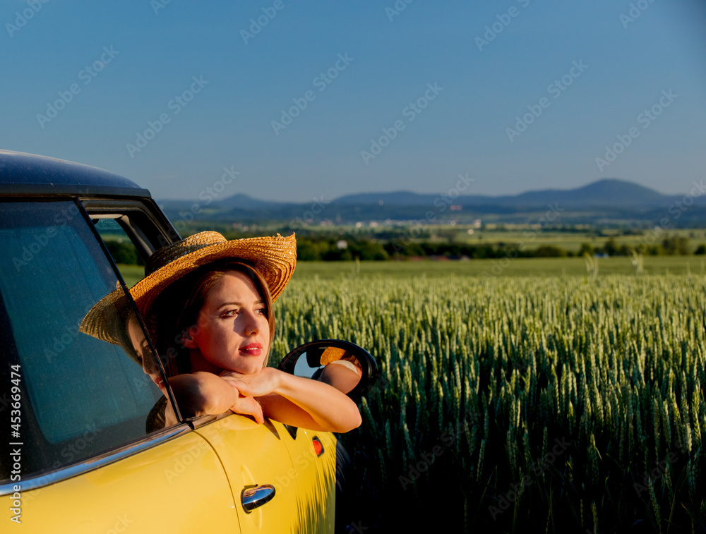 Wall mural young girl in a car on green wheat field