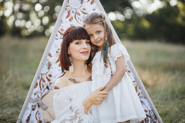 Portrait of happy native American mother and daughter at summer field. Woman and child wearing...