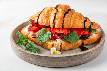 French croissant sandwich with fresh strawberries, cream cheese, mint and chocolate sauce on white...