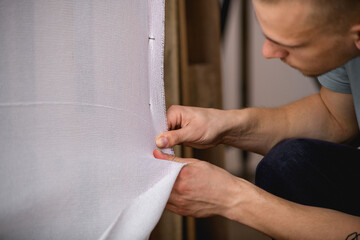 Young carpet maker fastening canvas on frame in workshop 