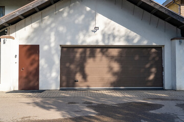 Modern brown garage with driveway and roller door. Family house with wide garage door with shadows...