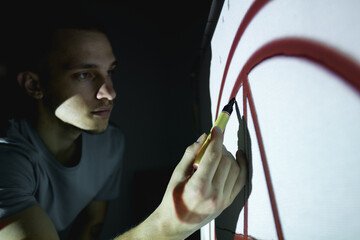 Young artisan drawing pattern with marker on white canvas in workshop 