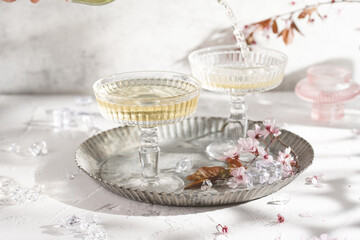 Two champagne glasses with splashes of champagne and pink cherry blossom on a grey surface