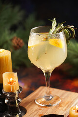 A big glass with christmas drink lemonade with rosemary and lemons surrounded by christmas decoration, lights and candles
