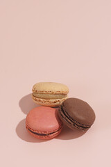 Three creamy, pink and chocolate macaron pastry stacked on top of each other - hard light on beige colored surface
