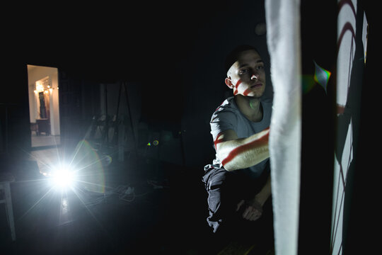 Young artisan working with carpet canvas near projector in dark workshop 