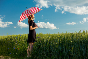 young girl in a black dress with a red umbrella on a green wheat field