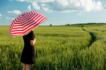 young girl in a black dress with a red umbrella on a green wheat field