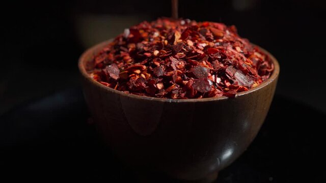 Crushed red cayenne pepper, dried chili flakes in a wooden bowl isolated on a dark background. Spinning cup with red peppers