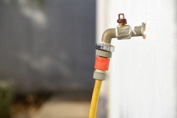An old garden hose is plugged into an old faucet sticking out of a white wall, outdoors