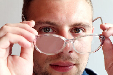 Fototapeta premium The concept of using glasses for vision . Glasses in the hands of a man on the background of the eyes, close-up