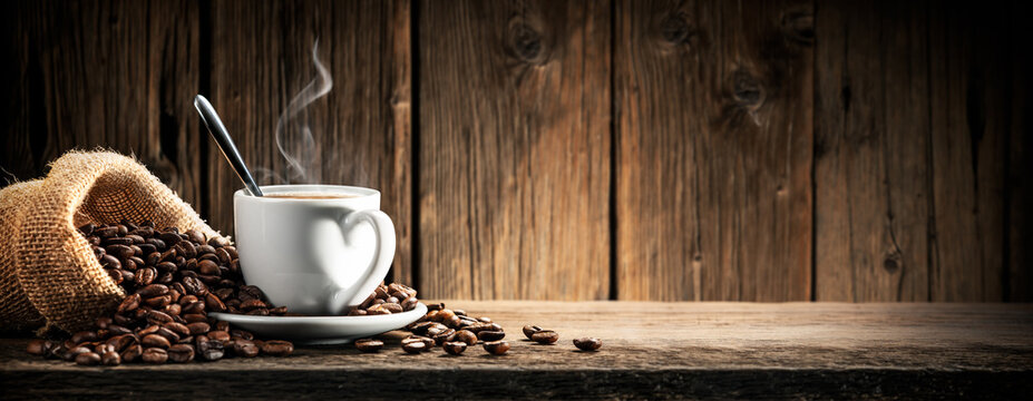 Small White Espresso Cup With Heart Shaped Handle On Wooden Table With Burlap Sack And Coffee Beans