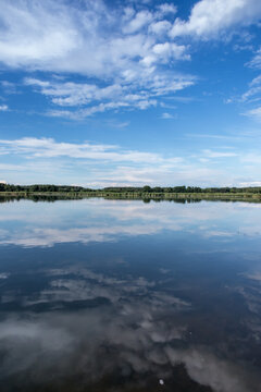 Blue sky covered with white clouds and sky reflection in the calm water of Pilka lake © rparys