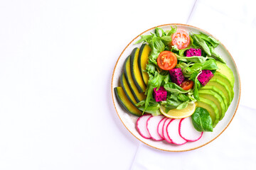 Healthy vegan salad fruits and vegetables dish with avocado, dragon fruit, radish, pumpkin, tomato, corn salad, lettuce, mizuna and lemon on white background