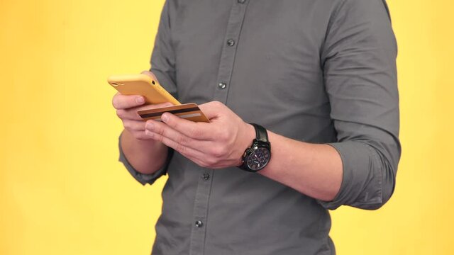 Close footage of man using credit card and smartphone over yellow background.